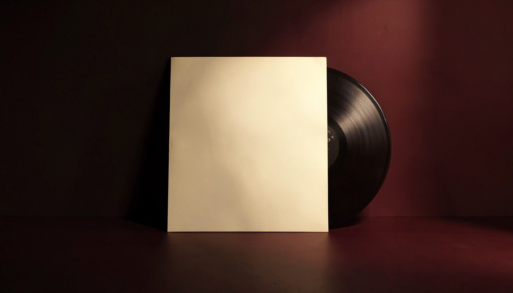 Vinyl record sleeve leaning against a dark wall, warm cream and deep maroon tones, soft directional light casting long shadows