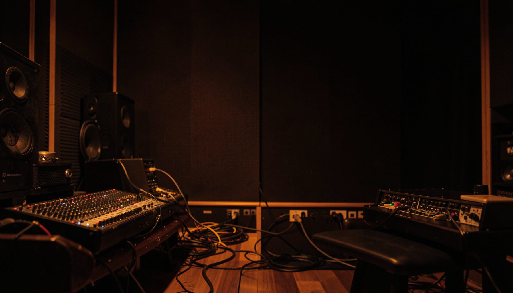 A softly lit studio scene with warm amber and deep brown tones, featuring audio equipment and cables against a dark background